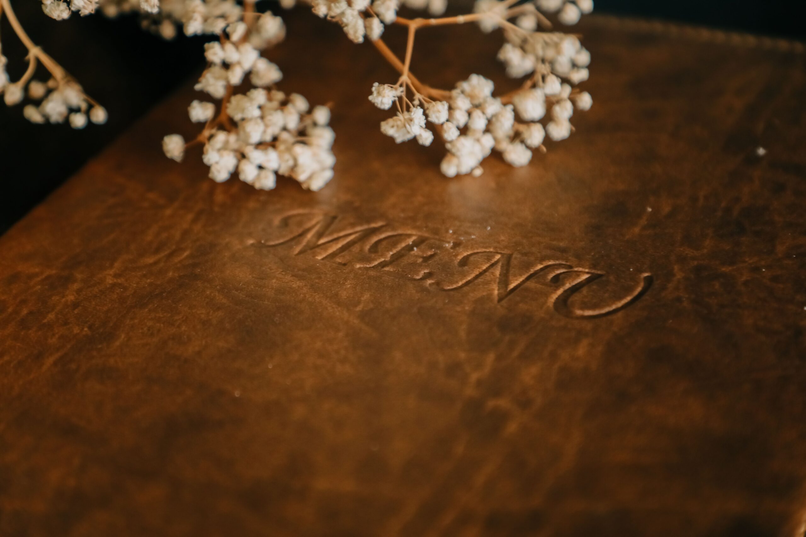 Close-up of a brown leather menu adorned with baby's breath flowers, perfect for upscale restaurant settings.