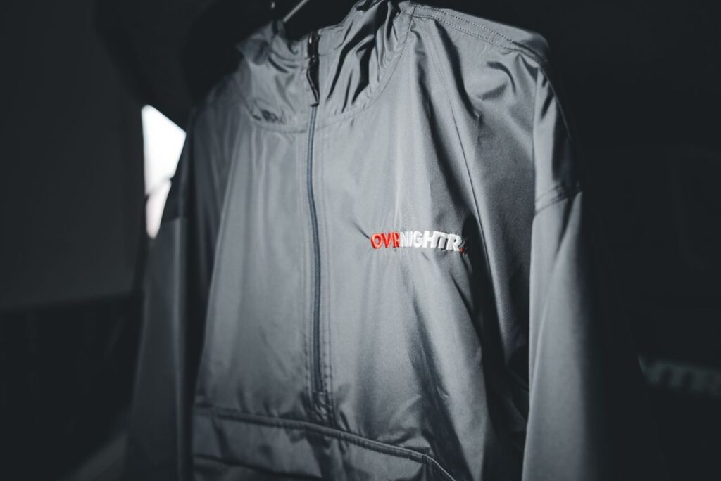 Gray windbreaker jacket with 'OVRNIGHTR' logo displayed in selective focus.