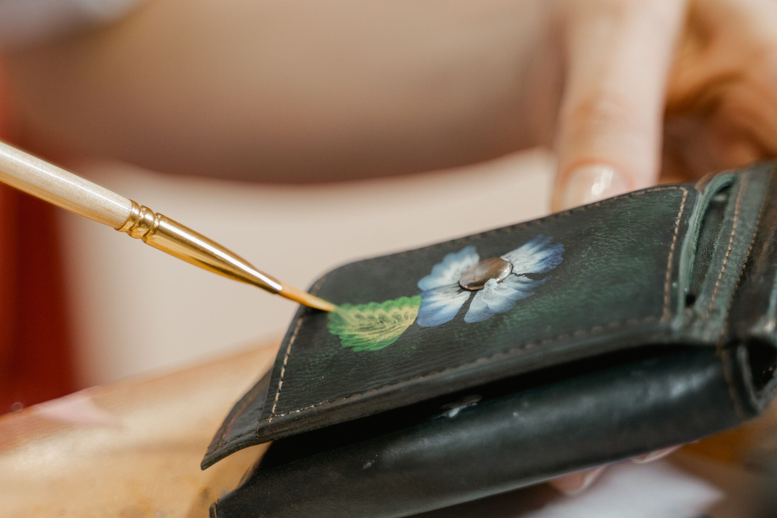 Artist hand-painting a delicate floral design on a leather wallet, showcasing craftsmanship.