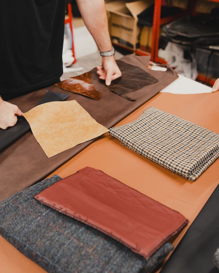 Tailor working with diverse fabric and leather samples on a table in a workshop.