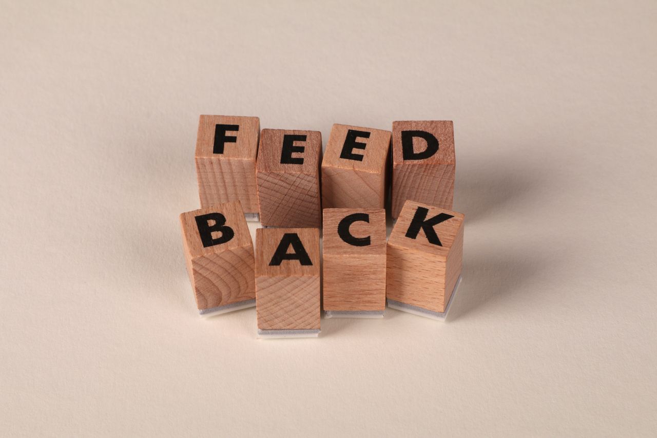 Wooden blocks arranged to spell 'Feedback' on a neutral beige background.