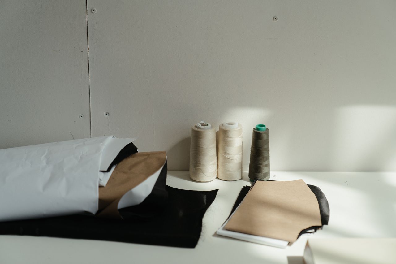 Arranged spools of thread and fabric pieces on a bright, sunlit table in a sewing workshop.