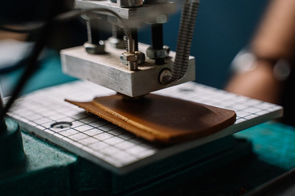 A close-up image showing a machine cutting leather in a workshop setting.