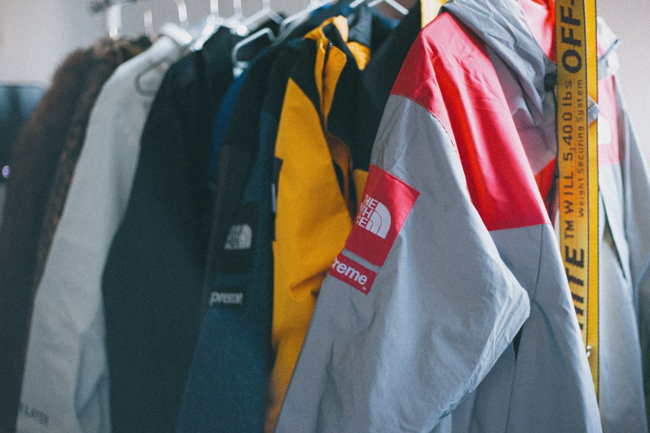 A collection of colorful Supreme jackets hanging on a clothing rack indoors.