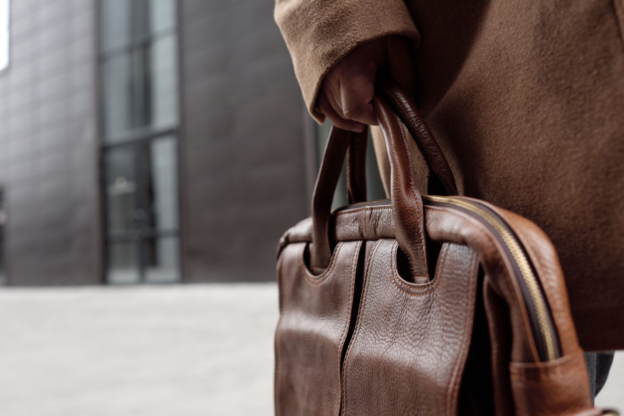 Close-up of a stylish leather briefcase being held by a person in winter attire.